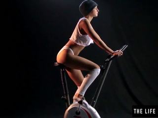 Ładniutka sweaty nastolatka skakanie na exercise bike siedziba.